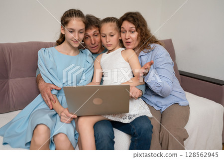 Family Laptop Togetherness: Indoors, family uses laptop for browsing, bonding on sofa during daytime. 128562945
