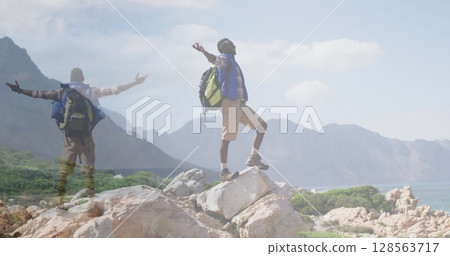 Composite of happy african american man hiking, and raising arms on mountainside 128563717