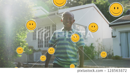 Image of smiley faces over happy african american boy in garden 128563872