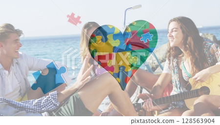 Image of colourful puzzle pieces heart over happy friends at summer beach party 128563904