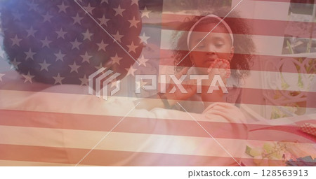 Image of flag of united states of america over african american mother cleaning daughters face 128563913
