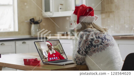 Image of snow falling over happy caucasian woman in santa hat on laptop image call 128564020