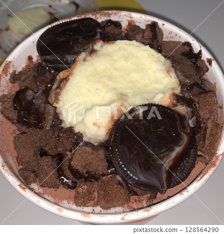 Rich and indulgent chocolate bingsu topped with chocolate syrup, brownie chunks, and chocolate shavings. A heavenly treat for chocoholics seeking a cool and creamy dessert escape. 128564290