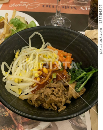 Bibimbap, a vibrant Korean rice dish topped with a variety of seasoned vegetables, gochujang, and a fried egg, often accompanied by sliced meat. Mixed together, it creates a flavorful and balanced. Bibimbap, a vibrant Korean rice dish topped with a variety of seasoned vegetables, gochujang, and a fried egg, often accompanied by sliced meat. Mixed together, it creates a flavorful and balanced. 128564295