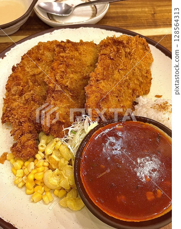 Crispy tonkatsu, a Japanese-style breaded and deep-fried pork cutlet, served with shredded cabbage and drizzled with savory sauce. A delightful balance of crunchy texture and juicy meat. 128564313