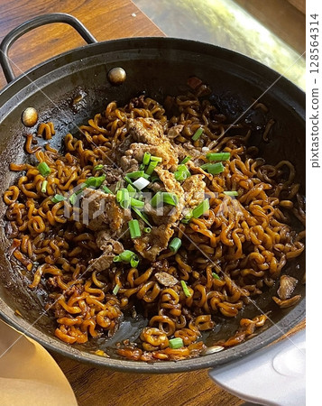 Savory jjapagetti noodles with a rich black bean sauce, topped with green onions and sesame seeds. A comforting Korean favorite that combines depth and flavor in each bite. 128564314