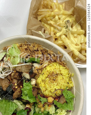 Colorful poke bowl with fresh fish, veggies, and rice served alongside crispy golden French fries an unexpected yet delicious fusion of clean, healthy bites and indulgent crunch. 128564324