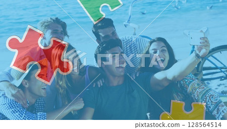 Image of colourful puzzle pieces over happy friends at summer beach party 128564514