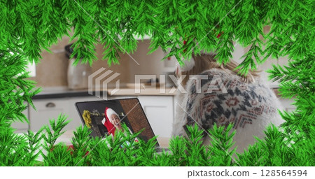 Green branches over woman wearing santa hat having a imagecall on laptop during christmas 128564594