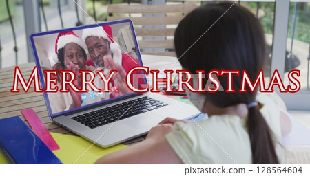 Image of merry christmas text over girl with face mask on laptop image call with family Image of merry christmas text over girl with face mask on laptop image call with family 128564604