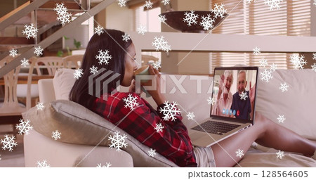 Image of snow falling over biracial woman on laptop image call with family at christmas 128564605