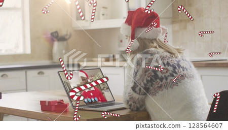 Image of candy canes falling over caucasian woman in santa hat on laptop image call at christmas Image of candy canes falling over caucasian woman in santa hat on laptop image call at christmas 128564607