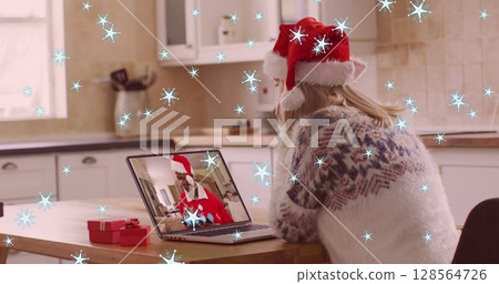 Image of snow falling over caucasian woman in santa hat on laptop image call at christmas 128564726