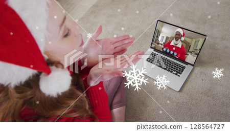 Image of snow falling over caucasian woman in santa hat on laptop image call at christmas 128564727