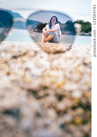 Smiling woman on beach viewed through sunglasses on sand, creative vacation summer concept 128564781