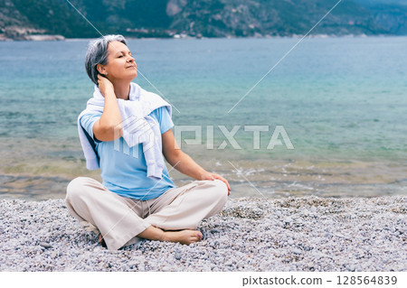 Mature Woman Enjoying Relaxation on Pebble Beach by Sea, Embracing Tranquility and Nature Mature Woman Enjoying Relaxation on Pebble Beach by Sea, Embracing Tranquility and Nature 128564839