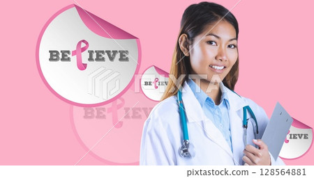 Image of believe text with pink ribbon over smiling biracial female doctor on pink background Image of believe text with pink ribbon over smiling biracial female doctor on pink background 128564881