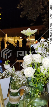 Rustic floral arrangement in jars. Festive decoration, white roses and plant branches in decorative jars. 128565006