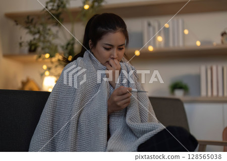 Health Awareness. Young woman feeling unwell and checking her temperature at home. Health Awareness. Young woman feeling unwell and checking her temperature at home. 128565038