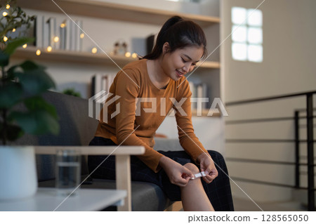 Health Awareness. Woman applying bandage to her knee at home. 128565050