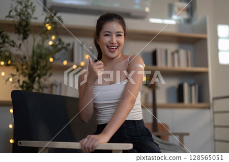 Positive Health. Young woman giving thumbs up after vaccination at home. 128565051
