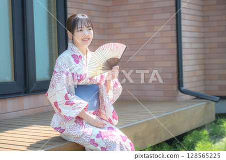 Woman in yukata with folding fan Woman in yukata with folding fan 128565225