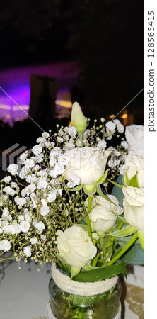 Rustic floral arrangement in jars. Festive decoration, white roses and plant branches in decorative jars. Rustic floral arrangement in jars. Festive decoration, white roses and plant branches in decorative jars. 128565415