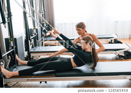 With the help of personal trainer. Women in fitness center are doing exercises With the help of personal trainer. Women in fitness center are doing exercises 128565459