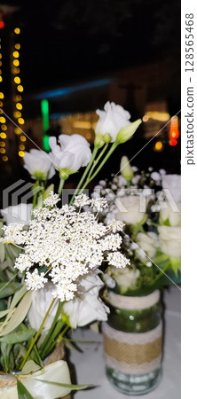 Rustic floral arrangement in jars. Festive decoration, white roses and plant branches in decorative jars. Rustic floral arrangement in jars. Festive decoration, white roses and plant branches in decorative jars. 128565468