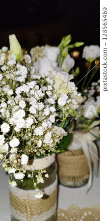 Rustic floral arrangement in jars. Festive decoration, white roses and plant branches in decorative jars. 128565469