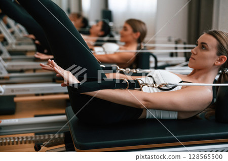 Lying down in a row and doing stretches. Women in fitness center are doing exercises Lying down in a row and doing stretches. Women in fitness center are doing exercises 128565500