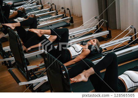 Lying down in a row and doing stretches. Women in fitness center are doing exercises 128565505