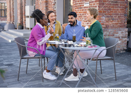 Friends enjoying sushi and drinks at an outdoor restaurant. They are eating and laughing together. 128565608