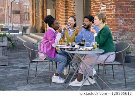 Friends enjoy a sushi meal outdoors on a sunny day, with smiles and chopsticks. Friends enjoy a sushi meal outdoors on a sunny day, with smiles and chopsticks. 128565612
