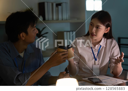 Collaboration and Communication. Young professionals discussing project details in a dimly lit office. 128565883
