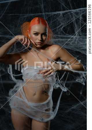 Red-haired woman entangled in a delicate net trap amidst a haunting web backdrop 128566196