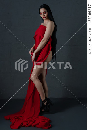 Elegant woman draped in flowing red fabric showcases beauty and allure 128566217