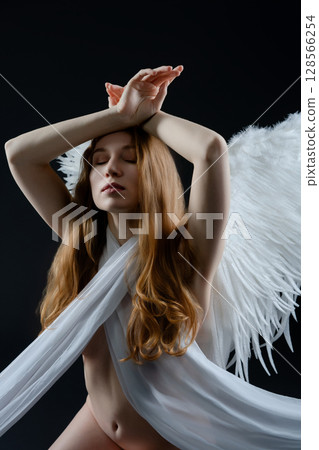 Red naked woman with angel wings posing gracefully in a studio setting Red naked woman with angel wings posing gracefully in a studio setting 128566254