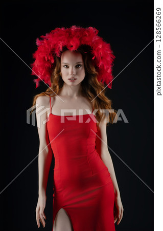 Woman posed in a striking red dress with a vibrant feathered headpiece showcasing strong emotions in a studio setting Woman posed in a striking red dress with a vibrant feathered headpiece showcasing strong emotions in a studio setting 128566269