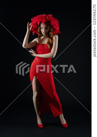 Woman posing gracefully in a vibrant red dress with dramatic feather headpiece in a studio setting Woman posing gracefully in a vibrant red dress with dramatic feather headpiece in a studio setting 128566270