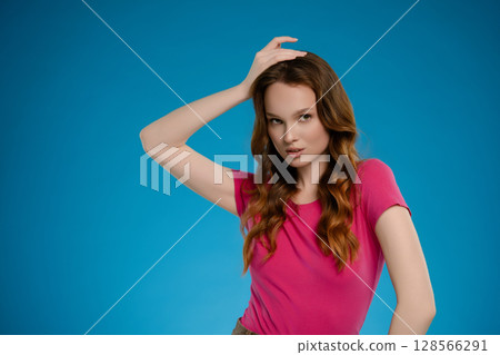 Woman expressing confidence and emotion while posing in a studio setting with a blue background during a creative photoshoot 128566291