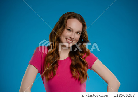 Woman posing in a studio environment, expressing joy and confidence with a vibrant blue backdrop 128566298