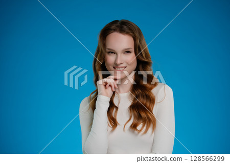 Woman posing with a playful expression against a bright blue background in a studio setting Woman posing with a playful expression against a bright blue background in a studio setting 128566299