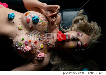 Woman with body art and candy inspired features lying on a dark surface Woman with body art and candy inspired features lying on a dark surface 128566325