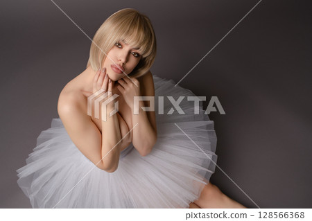 Elegant woman modeling in lingerie with a tulle skirt against a neutral backdrop Elegant woman modeling in lingerie with a tulle skirt against a neutral backdrop 128566368