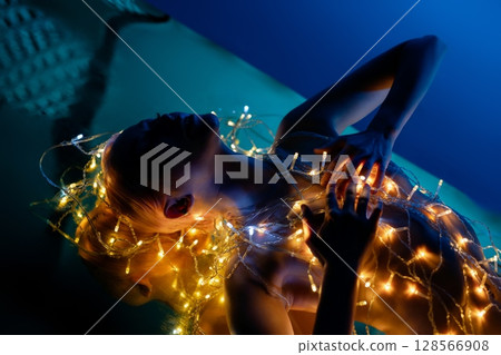 Elegant topless woman surrounded by soft glowing lights in intimate setting 128566908