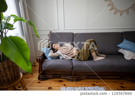 Quiet lazy woman lounging on sofa at home alone, lost in thoughts with indifferent mood, idleness 128567660
