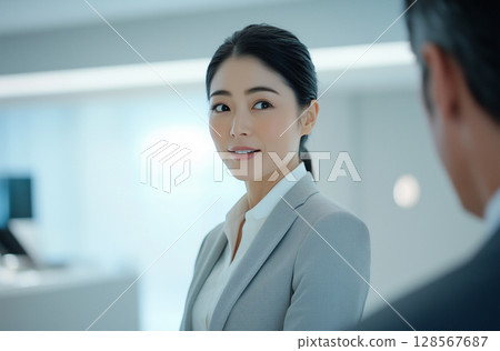 A businesswoman in a suit conversing with a colleague at work: "generative AI" 128567687