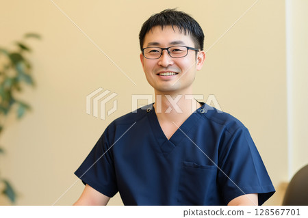 A generative AI of a smiling male medical worker in medical wear sitting A generative AI of a smiling male medical worker in medical wear sitting 128567701