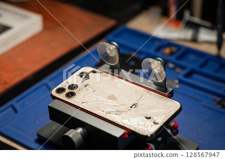 Broken smartphone in a repair service with shattered glass placed on a workspace for assessment and fixing during daylight hours 128567947